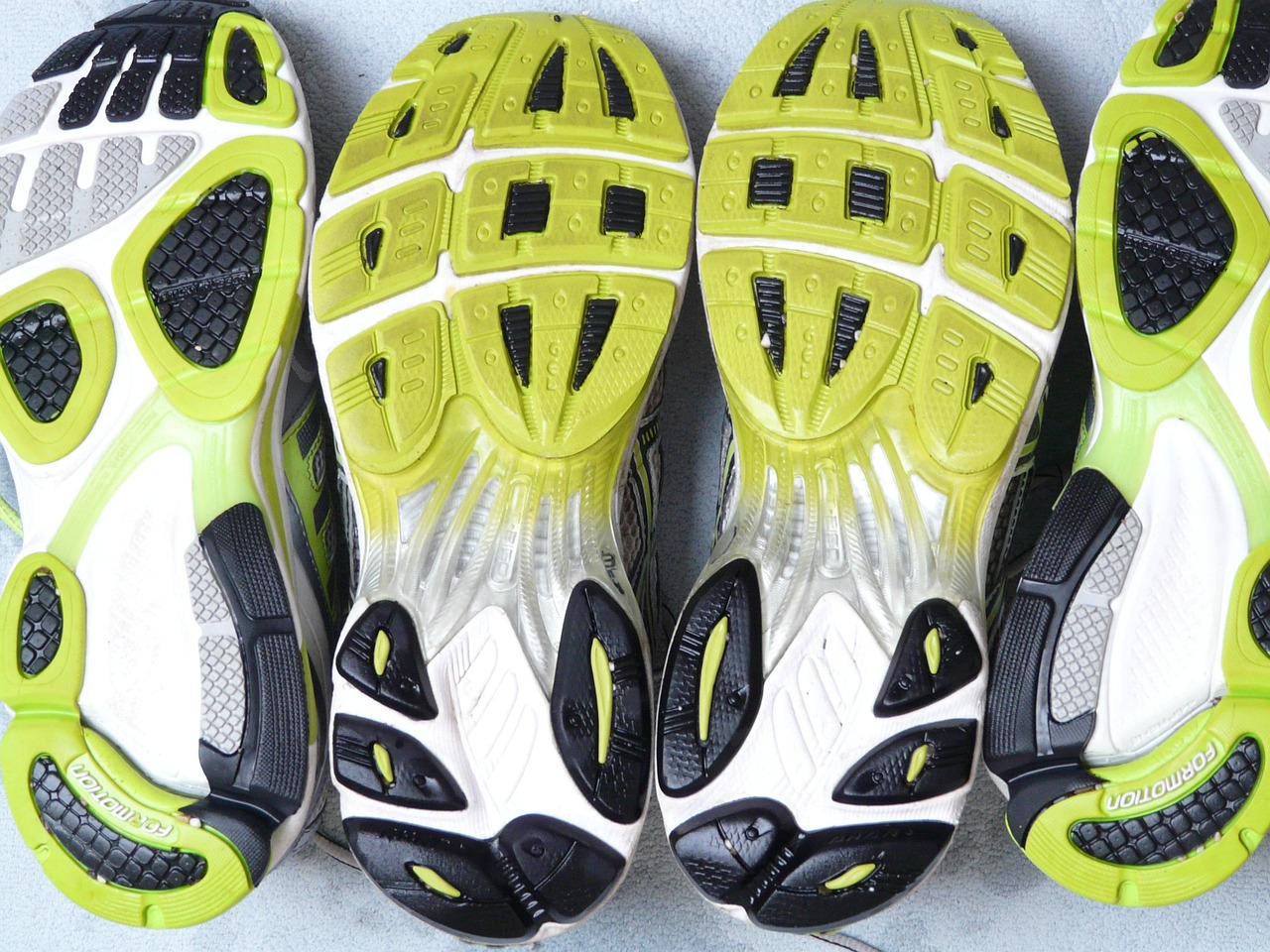 Vier Laufschuhe mit unterschiedlichem Sohlenprofil von unten nebeneinander fotografiert