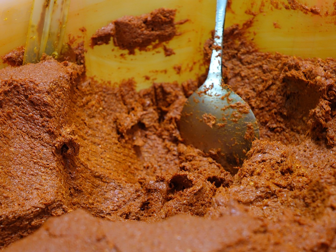 Red Thai-style curry paste being ground with a mortar and pestle alongside whole spices.