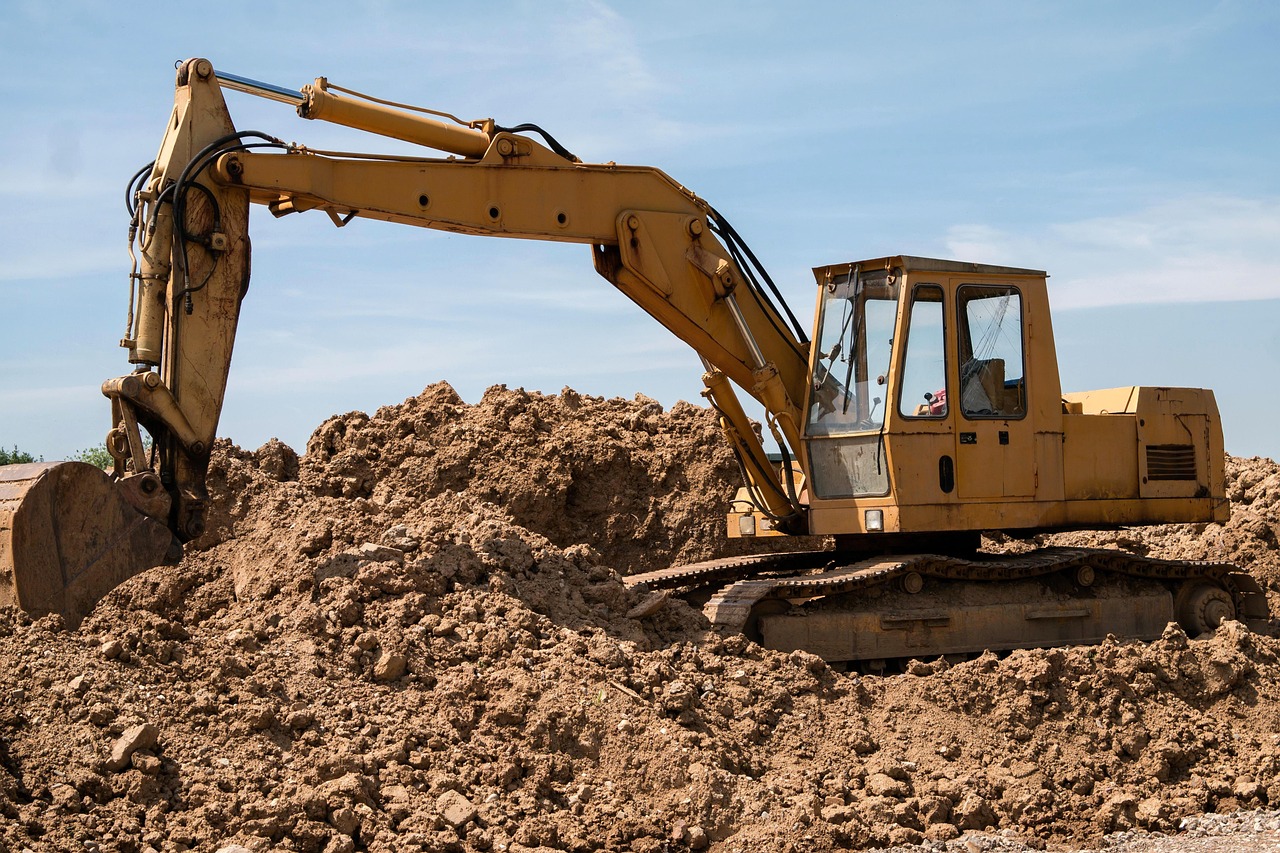 Yellow excavator at a construction site, captured from ground level against a clear sky.