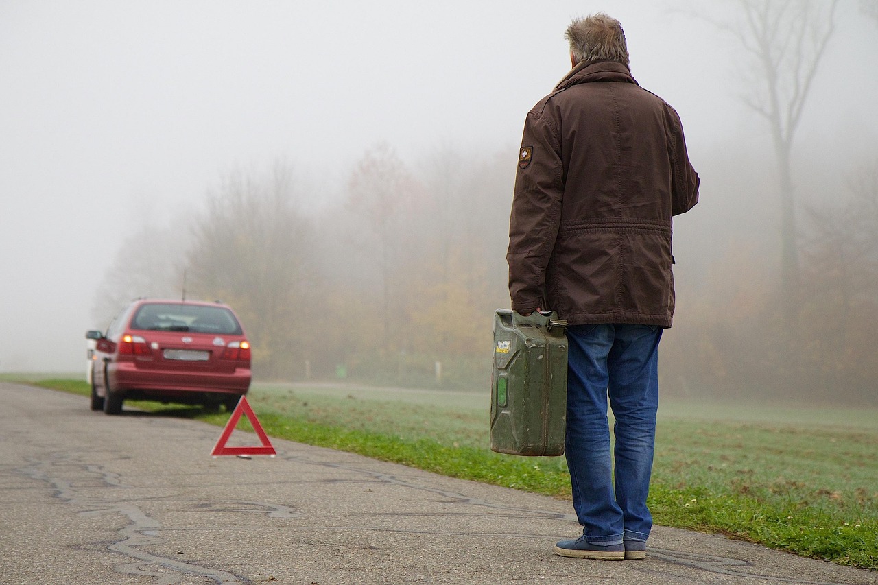 Driver standing beside a broken-down vehicle on a roadside, with a warning triangle placed behind it.