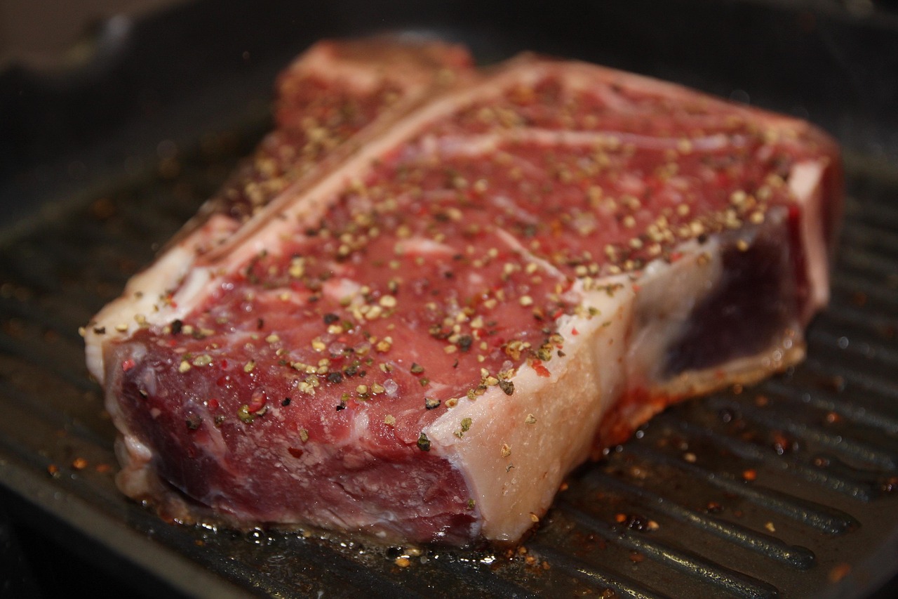 Raw porterhouse steak on a wooden cutting board showing the T-shaped bone with strip loin and tenderloin sections