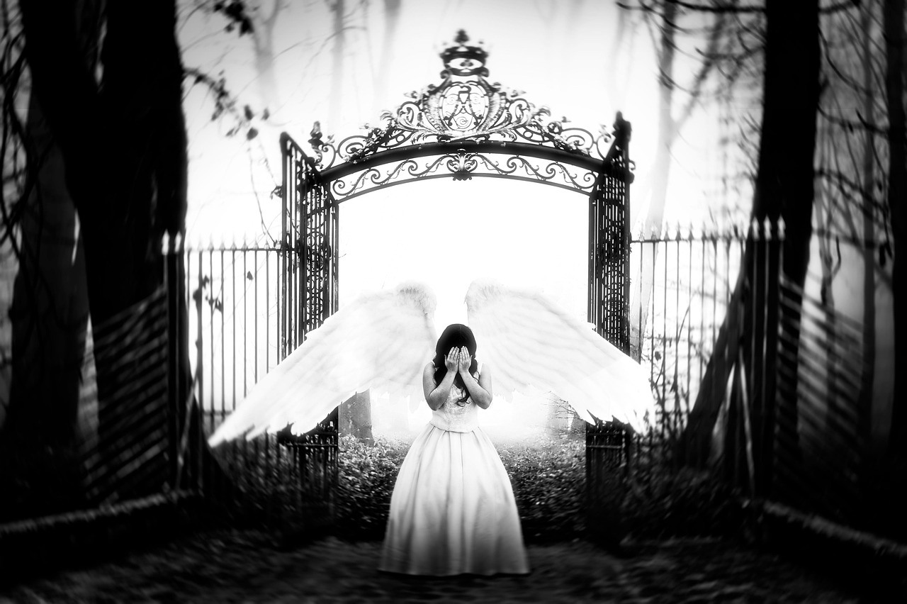 Stone angel statue beside an open iron gate outdoors.