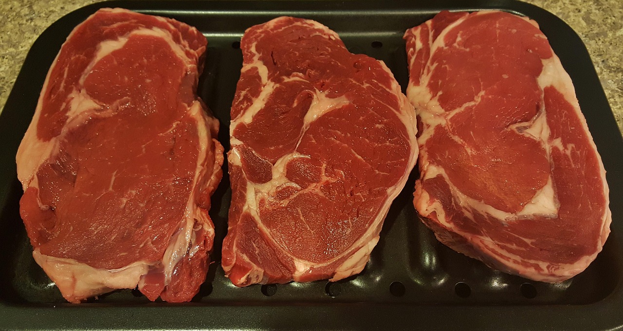Two thick raw ribeye steaks on a butcher block showing intense intramuscular marbling and the ribeye cap muscle