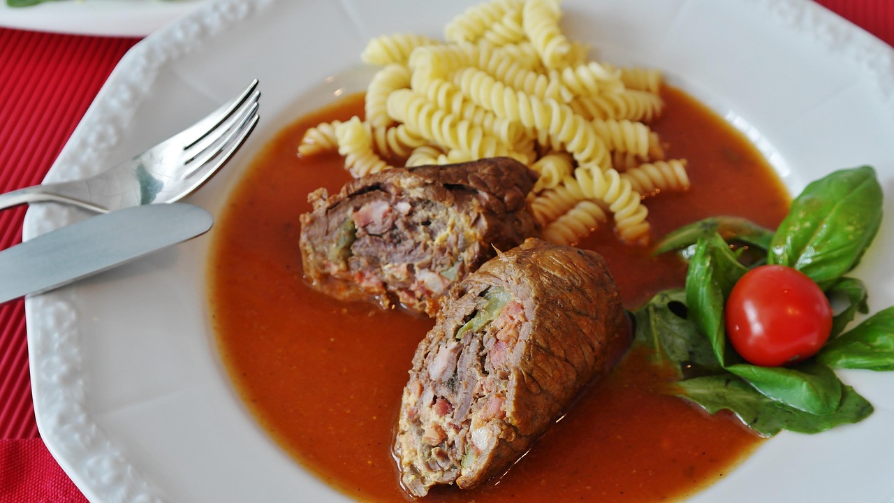 Beef roulades braising in a pan — the classic rolled and tied shape of braciole before the sauce reduces around them.