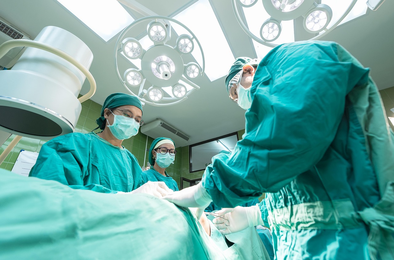 Surgeons in scrubs and gloves performing an operation in a hospital.