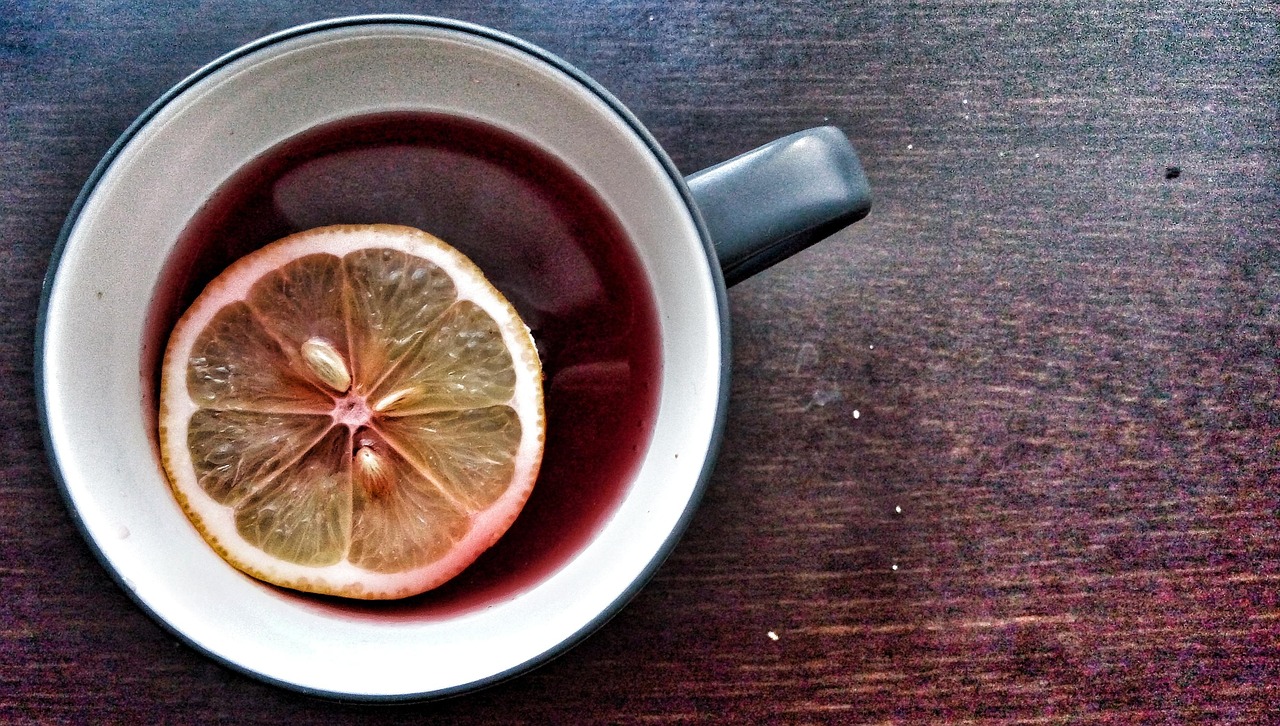 Glass cup of hot tea with a lemon slice on a saucer.