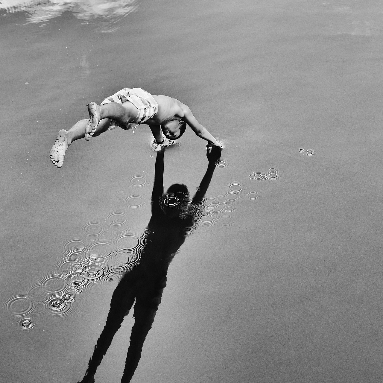 Person leaping toward a calm water surface, arms outstretched, with a shadow reflected below.