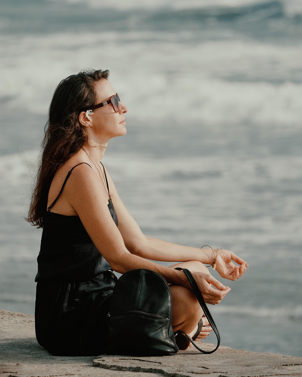 Woman standing at the edge of a Bali beach with waves washing around her feet at golden-hour sunset