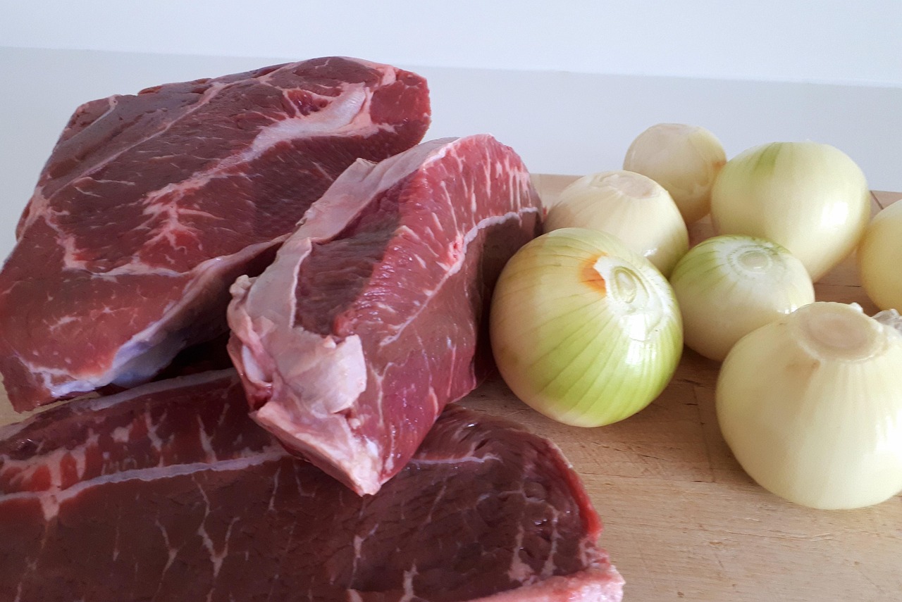 Overhead view of a slow cooker filled with browned beef cubes, carrots, onions, bacon and dark rich broth ready to cook