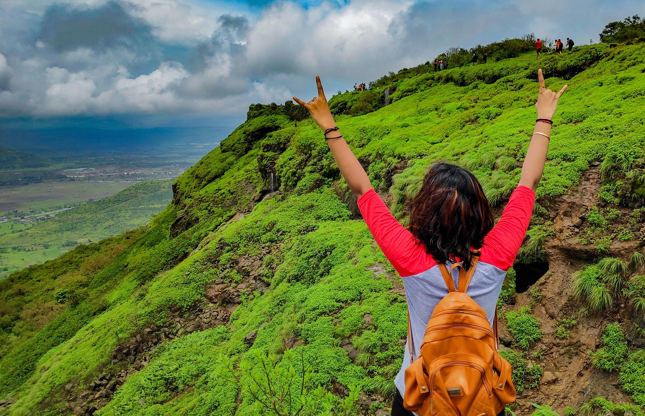 A trekker on a bright green Sahyadri hillside in the monsoon, looking out over a misty valley in Maharashtra