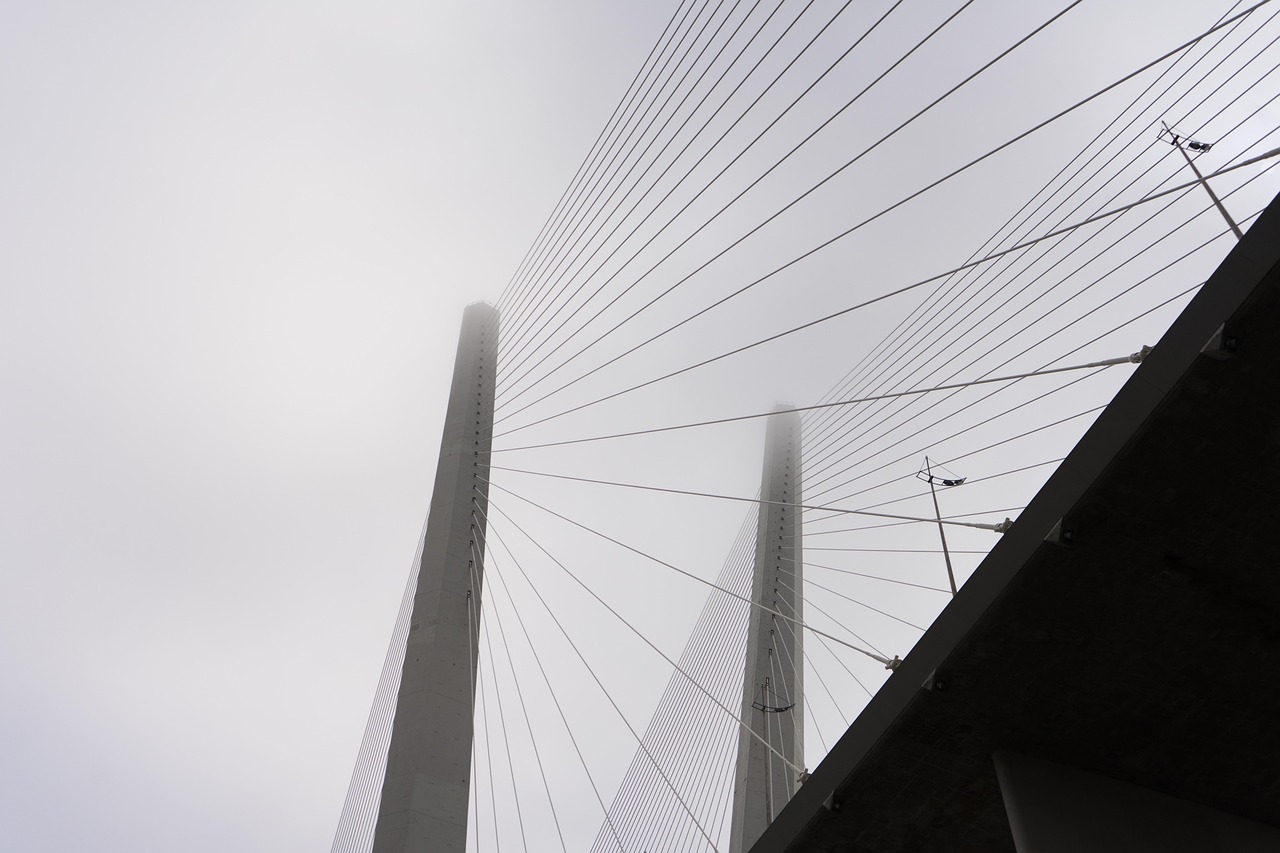 Cable-stayed bridge with tall concrete pillars photographed from below against a bright sky.