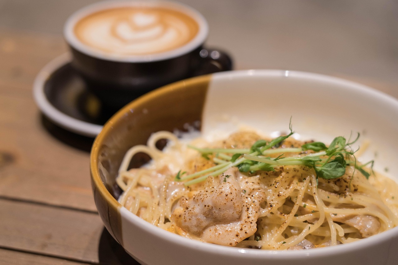 Bowl of creamy pasta topped with pieces of cooked chicken and fresh green herbs