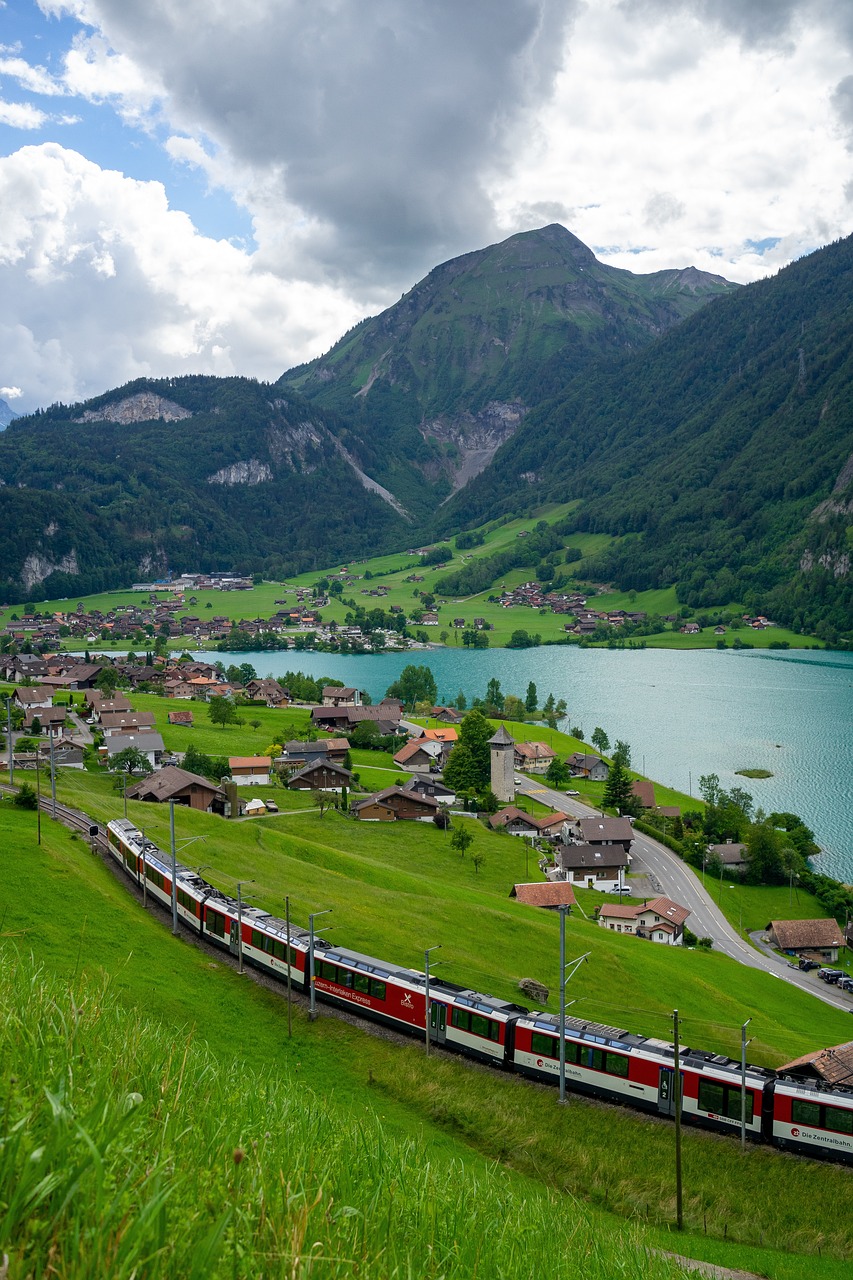 Picturesque Swiss mountain village with traditional alpine chalets, church steeple, green meadows and dramatic snow-capped peaks under blue sky with white clouds.