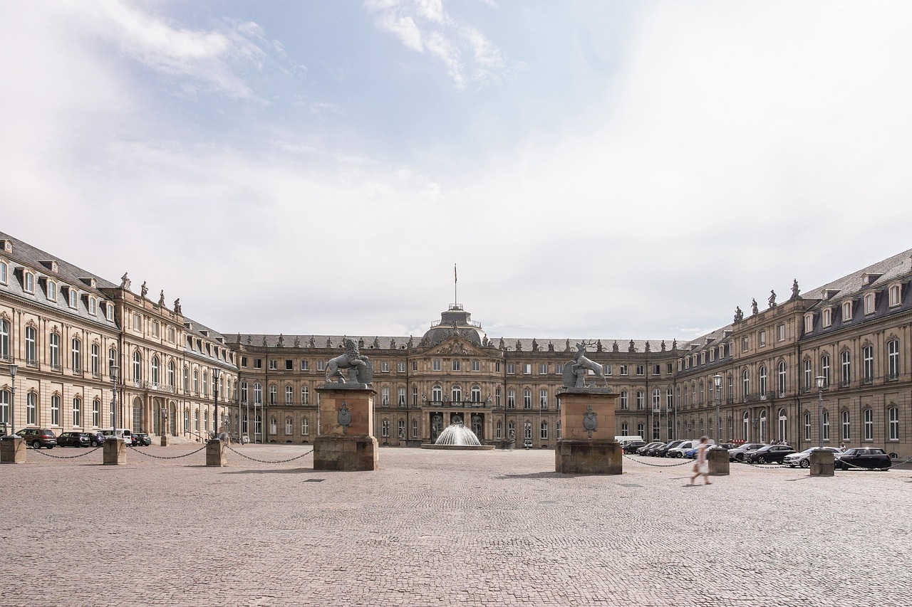 Grand baroque palace courtyard with symmetrical wings, central fountain, and stone statues under a bright sky in Germany