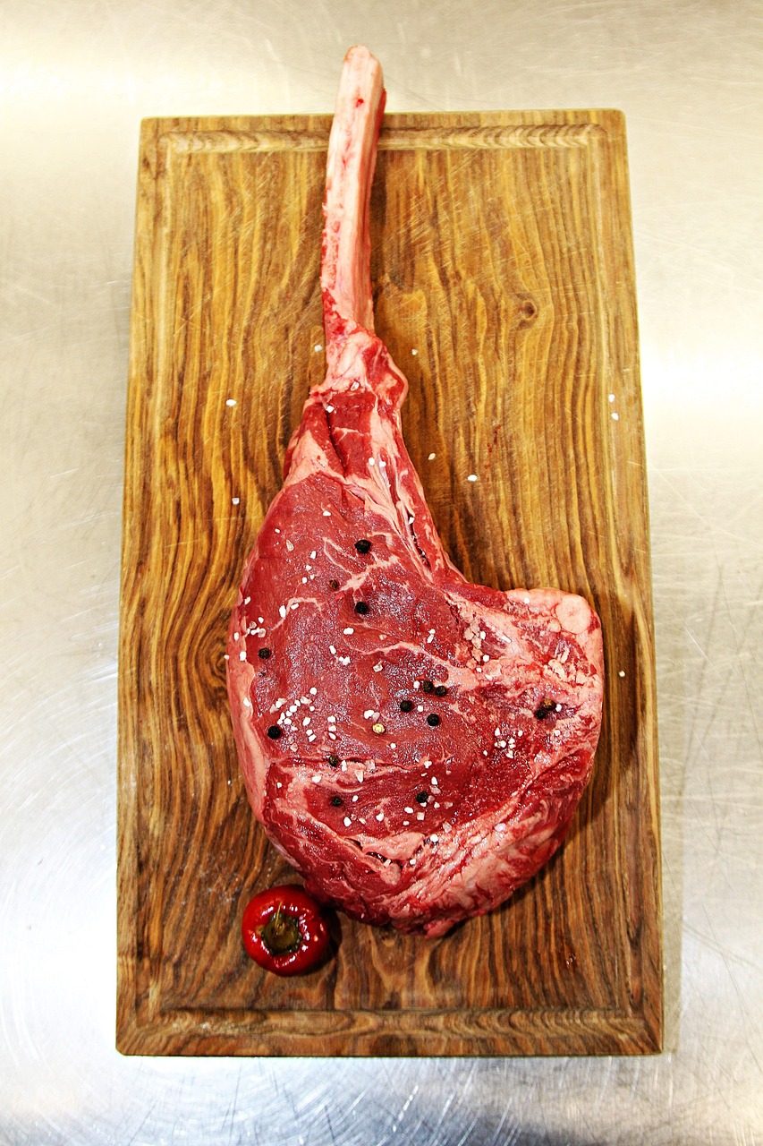 Raw tomahawk ribeye on a wooden cutting board showing marbling, fat cap and long bone