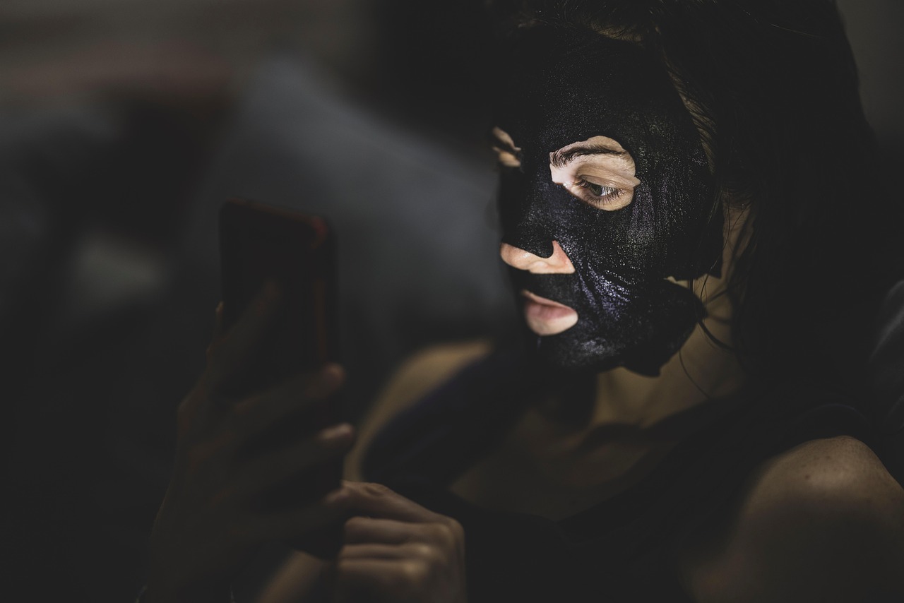 Woman wearing a black sheet mask while looking at her phone at night