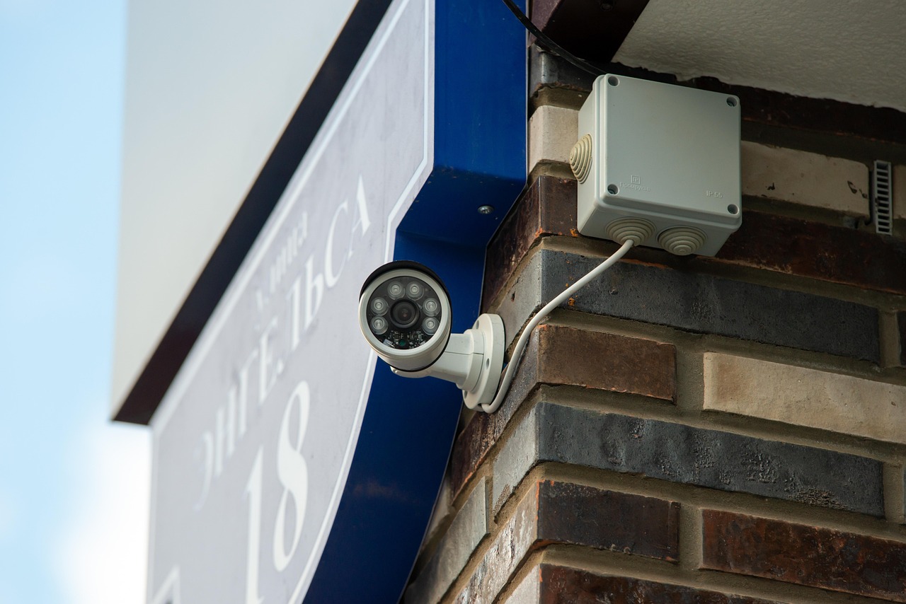 Close-up of a black security camera mounted outdoors against a light sky.