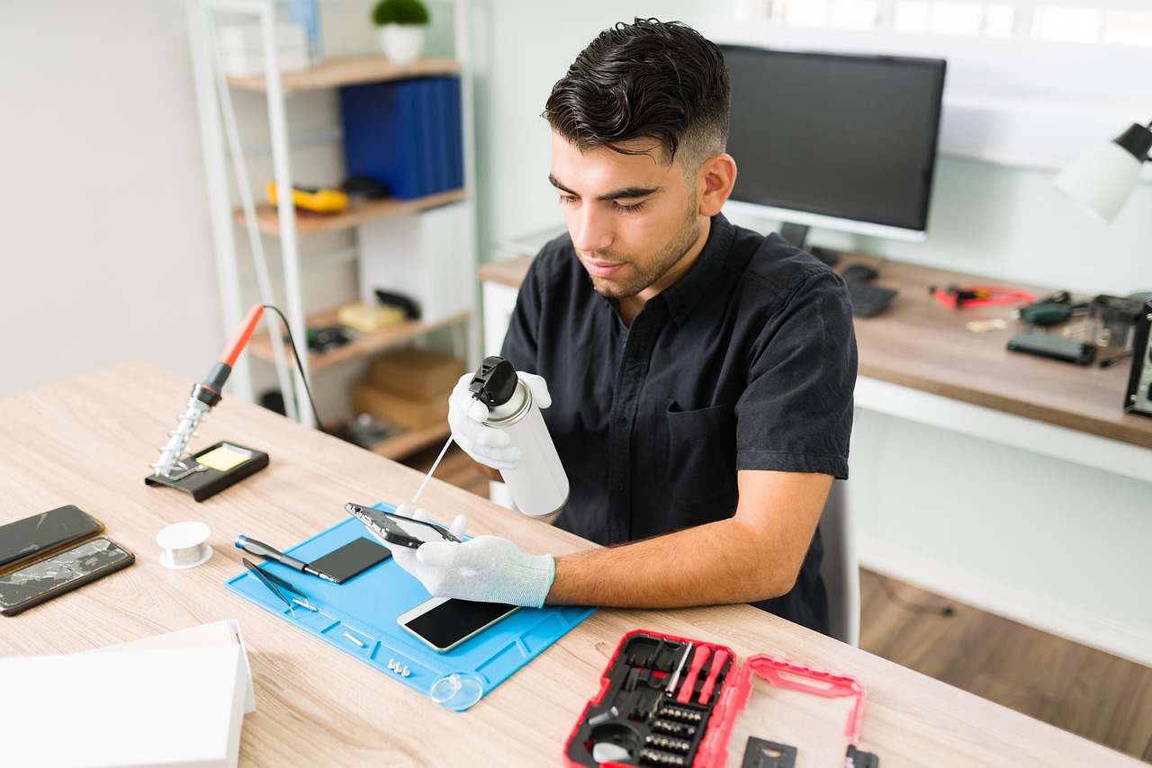 A repair technician holding a smartphone with a cracked screen in a repair workshop