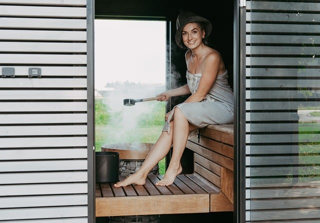 sauna, sauna heater, sauna stones, sauna steam, electric heater, sauna house, sauna design, sauna inspiration, nordic design, safety, safety railing, sauna safety, woman in sauna, sitting in sauna, laughing, person in sauna, sauna bench, pouring water, hive heater, hive mini heater, sauna hat