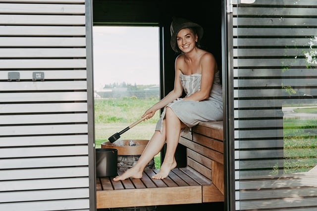 sauna, sauna heater, sauna stones, sauna steam, electric heater, sauna house, sauna design, sauna inspiration, nordic design, safety, safety railing, sauna safety, woman in sauna, sitting in sauna, laughing, person in sauna, sauna bench, pouring water, hive heater, hive mini heater, sauna hat