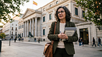Random: ai generated, woman, outdoors, office building, people, sidewalk, autumn, spanish flag, architecture, historic building, notebook, atmosphere, bag, autumn fashion, formal wear, metal railing, glasses, career, record, monitor, city